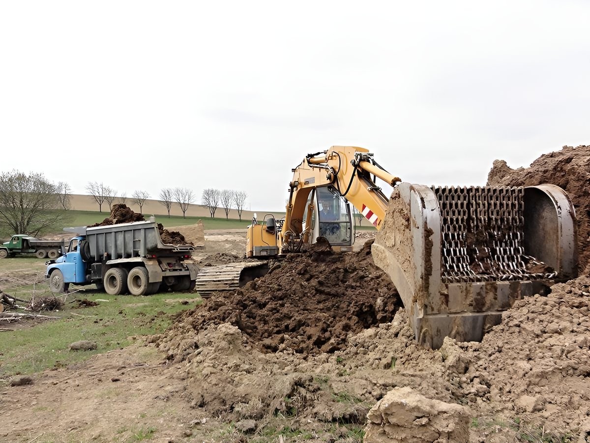 Pásový bagr Liebherr se širokými pásy nakládá výkopek na sklápěč při stavbě rybníka